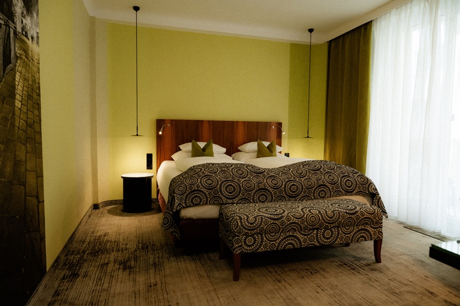 Helles, modernes Hotelzimmer mit Doppelbett und dekorativen Kissen, zeitgemäßer Beleuchtung und einladender Atmosphäre.