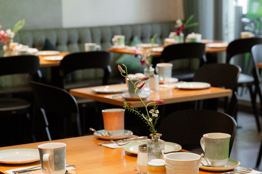 Gedeckter Tisch mit Tellern, Besteck und kleinen Blumenarrangements im Restaurantbereich