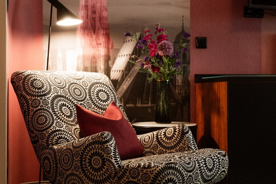 Gemusterter Sessel neben einem kleinen Tisch mit einer Blumenvase vor einer Stadtansicht